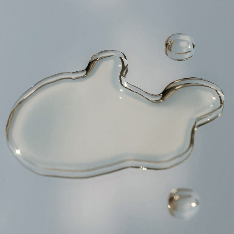 clear liquid serum puddle and droplets on a reflective surface showing skincare product texture
