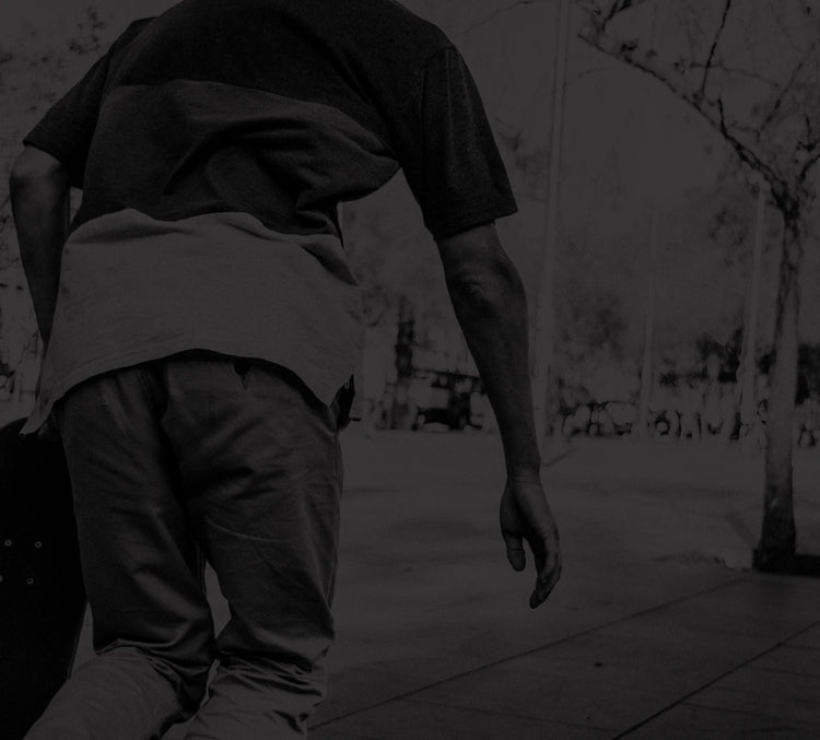 Skateboarder from behind holding a board in an outdoor park with trees in black and white