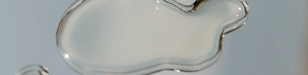Clear viscous skincare serum droplet with a glossy texture on a light blue background