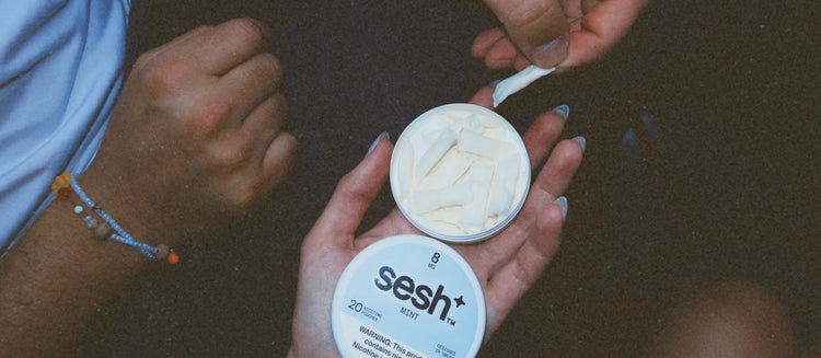 Person holding an open tin of sesh+ mint nicotine pouches while another person takes one out.